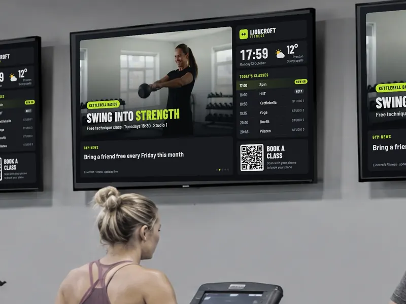 Gym wall screen with a split-screen layout: workout video, class timetable, clock and weather